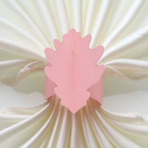 Détail d'un rond de serviette en papier nacré rose en forme de feuille sur satin blanc