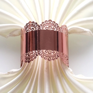 Close-up of rose gold laser-cut lace napkin ring on a white satin napkin for weddings