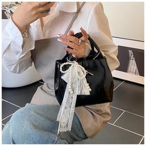 Detail of a black patent leather handbag featuring a white lace pearl bow charm
