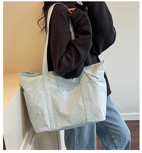 Detail view of large light blue canvas tote bag with functional pockets on a model shoulder