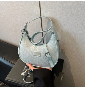 Detail of light blue hobo bag with woven texture, metal logo, and adjustable strap