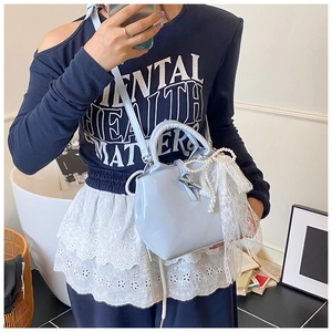 Close-up of light blue patent leather handbag with lace bow and pearl chain detail