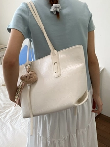 Minimalist white crocodile texture tote bag with plush bear charm on female model shoulder