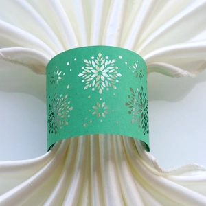 Macro detail of green laser-cut snowflake napkin ring on white satin fabric