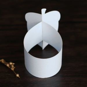 Close-up of white paper butterfly napkin ring on a dark wood texture background