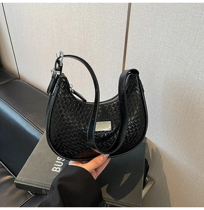 Detailed view of woven texture and silver metal plaque on black hobo crescent bag