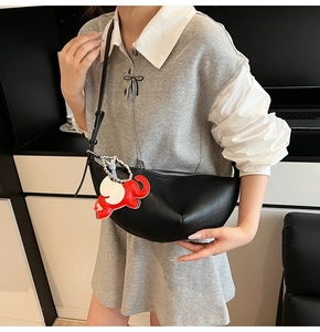 Detailed view of black crescent leather bag with red elephant charm on model