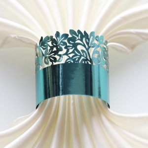 Close-up of a teal blue hollowed metal napkin ring with leaf pattern on satin