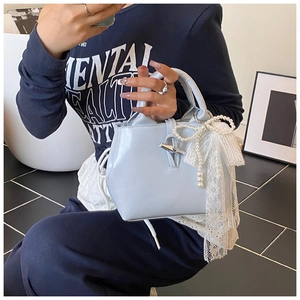 Detail of light blue leather handbag featuring silver horn clasp and lace bow charm