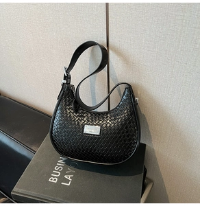 Detail view of black woven hobo bag texture with silver metal plate and leather strap