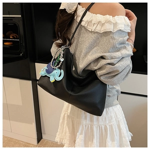 Detail of black leather hobo bag with pebble texture and cute blue elephant pendant charm