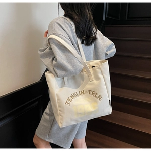 Détail d'un grand sac cabas en toile avec lettrage porté sur un escalier en bois