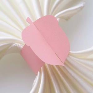 Detailed view of pink leaf-shaped paper napkin ring on a white satin cloth
