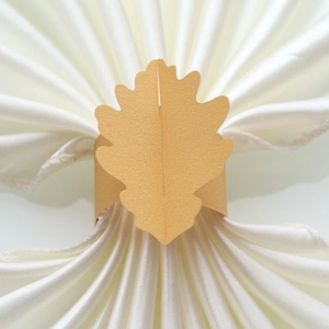 Vue détaillée d'un anneau de serviette en forme de feuille dorée sur du satin blanc