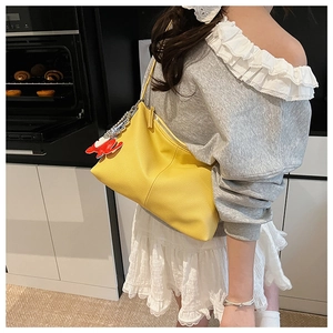 Detail of yellow pebbled leather tote bag featuring a fish charm and metal zipper
