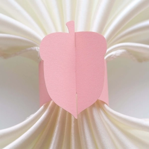 Macro view of a matte pink acorn-shaped cardstock napkin ring on white satin cloth