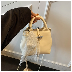 Detail of a creamy white handbag with elegant pearl and lace charm and top handle