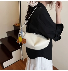 Detail of white lychee leather dumpling bag with brown elephant charm on model