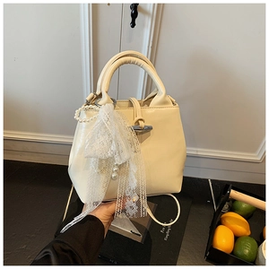 Detailed view of cream leather handbag featuring a delicate lace bow and pearl charm