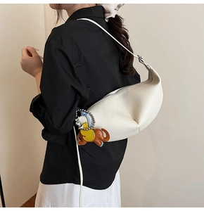 Detail of off-white leather crescent bag with elephant charm on model in cream setting