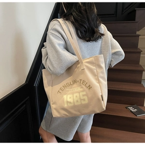 Grand sac cabas en toile beige avec lettrage, porté à l'épaule dans une scène de style de vie