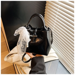 Detail of black glossy bucket bag featuring metallic toggle closure and pearl lace charm