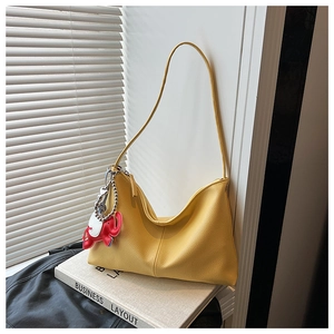 Close-up of yellow lychee grain leather handbag with a red elephant charm ornament