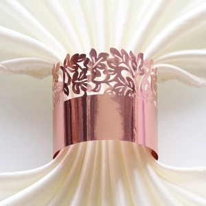 Close-up of laser-cut rose gold napkin ring with floral hollow pattern on satin fabric