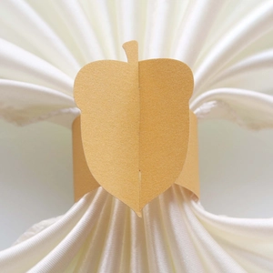 Detail of acorn shaped paper napkin ring on a white satin fabric for table decor