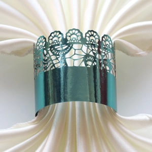 Detail of metallic teal laser-cut crown napkin ring on white satin fabric