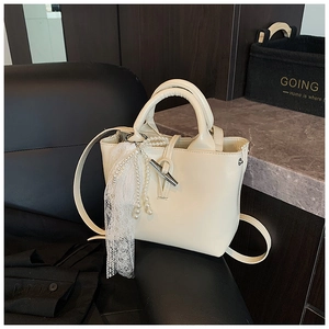 Detail of cream off-white handbag with matte leather, metal horn buckle, and pearl lace charm
