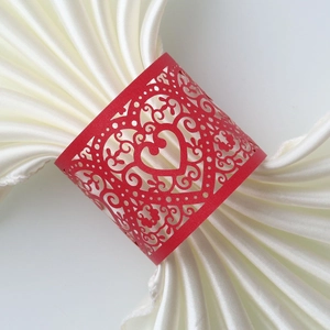 Detail of red laser-cut heart napkin ring with ornate scrollwork on white silk fabric