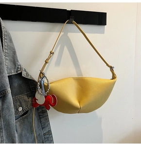 Detail of yellow dumpling bag with elephant charm on white background and denim jacket