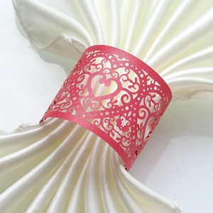 Macro detail of red laser-cut heart pattern napkin ring on white satin fabric