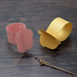 Detail of elegant acorn paper napkin rings in pink and gold on a dark wood table