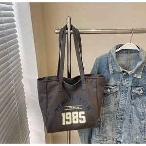 Gros plan du sac cabas en toile gris anthracite avec lettrage vintage sur un cintre