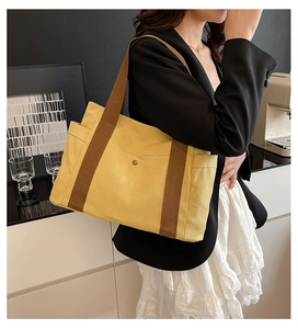 Detail of yellow canvas tote bag featuring brown woven handles and practical side pocket
