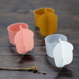 Macro detail of acorn-shaped paper napkin rings in pink and mustard on wood surface