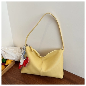 Detail of yellow lychee grain leather tote bag with cute cartoon elephant charm on wood surface