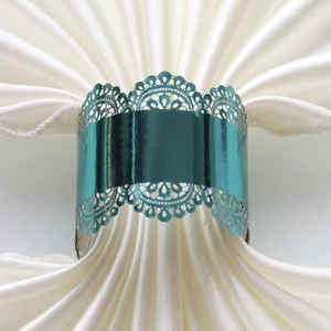 Detailed view of teal metal hollow lace napkin ring on elegant white satin fabric