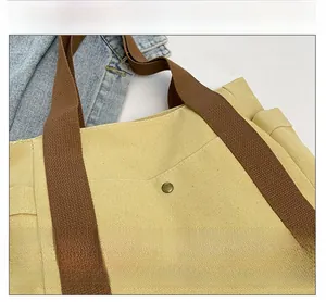 Detail of yellow canvas tote bag with thick brown strap and vintage metal rivet