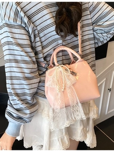 Pink crossbody handbag with lace bow and pearls shown from a side view by a model