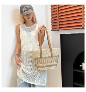 Detailed view of woven straw tote bag with brown leather handles worn by a fashion model