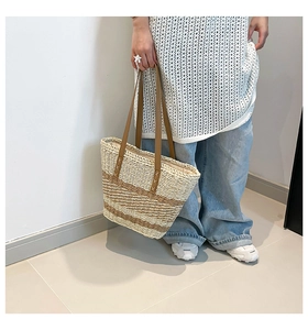 Detail view of woven straw tote bag with brown leather handles and striped texture