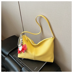 Detail of yellow pebbled leather tote bag featuring a cute red elephant charm on a bench