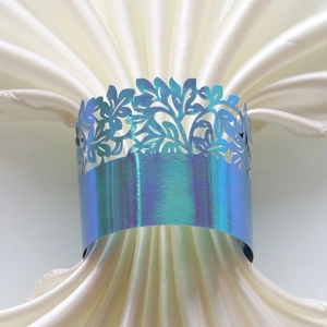 Close-up of laser-cut iridescent napkin ring with floral pattern on white silk fabric
