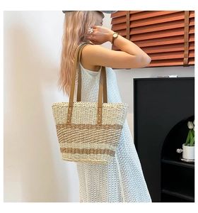 Detailed view of woven tote bag with beige and brown stripes and leather handles worn by model