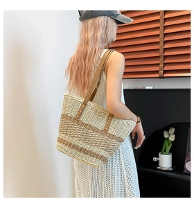Detail of striped woven tote bag with brown leather straps worn on shoulder