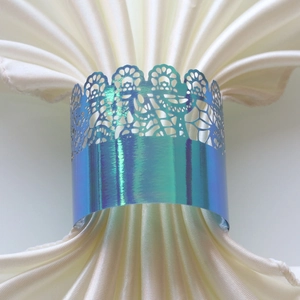 Close-up of laser-cut holographic blue lace napkin ring on a white satin cloth