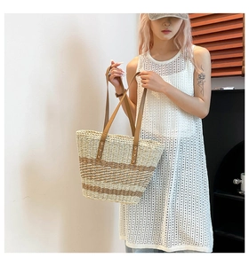 Detail of woven straw tote bag featuring brown faux leather handles and white dress